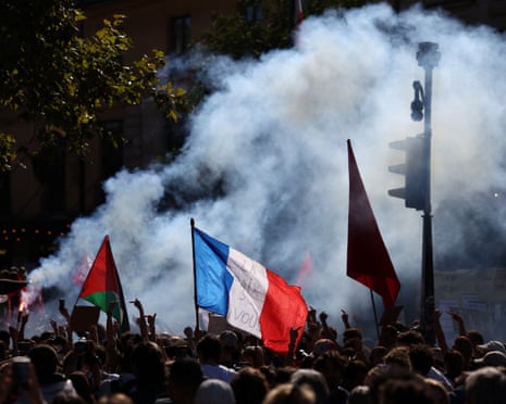 A tricolour flag above a crowd, with smoke in the background