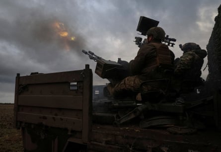Soldiers fire a large gun into the sky in dim light