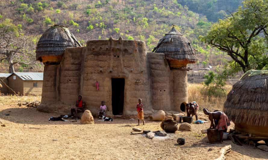 A family sitting outside a mud house with thatched towers