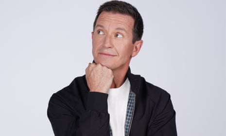 Comedian Rove McManus in a black jacket posing with his chin resting on a closed fist, against a light grey background.