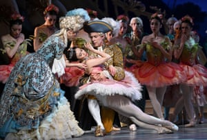 A dancer is held by another dancer in front of the corps de ballet during a performance