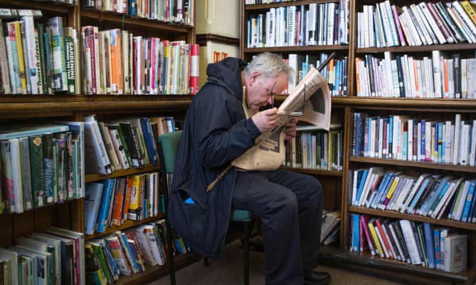 A short sighted man reading a newspaper in the old Aberystwyth Carnegie funded public lending library, Wales UK