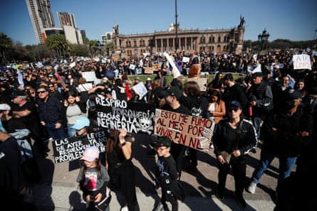 a large crowd of people holding signs in spanish protest a refinery