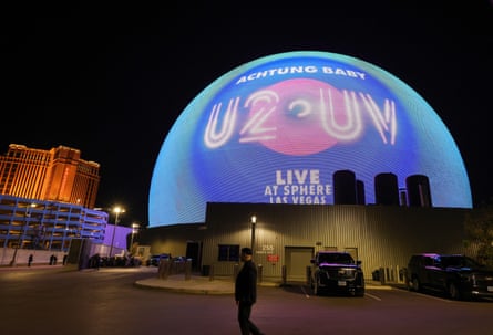 A person walks in front of the round Sphere venue covered in a promotion for the U2 show