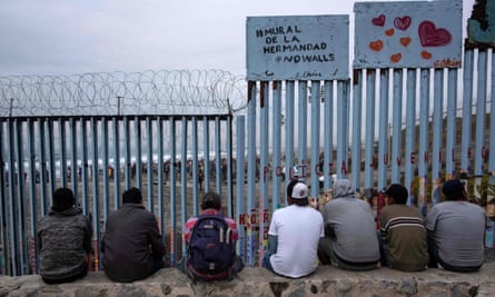 Men sit next to a sign reading ‘mural of brotherhoood’ look at the US-Mexico border fence from Playas de Tijuana in Baja California.