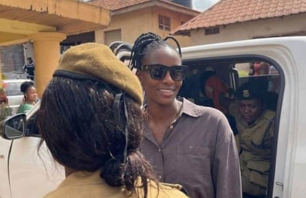 A young African woman in sunglasses gets out of a 4x4 escorted by soldiers