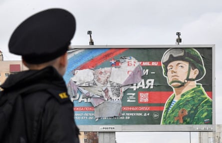 Курсант стоит перед рекламным щитом, рекламирующим военную службу по контракту в Санкт-Петербурге, Россия.