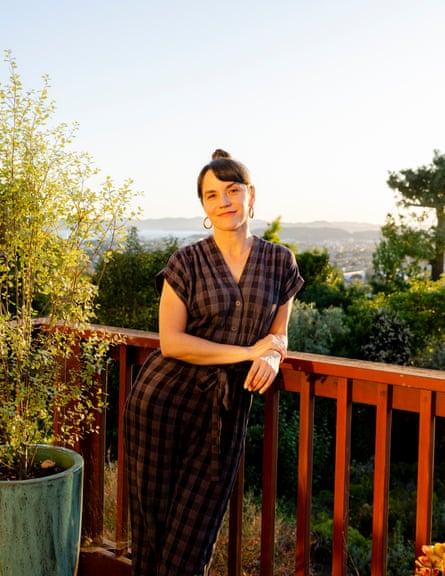 A woman wearing a bun and a plaid dress poses outside on a deck