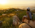 Rear view of woman hiker sitting on rock on top of hill while looking at sunset over San Diego California