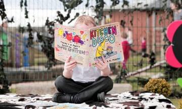A young child reads a book outside at a nursery school