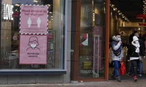 A shop window with big pink and white signs in the windows and two people in face masks standing outside