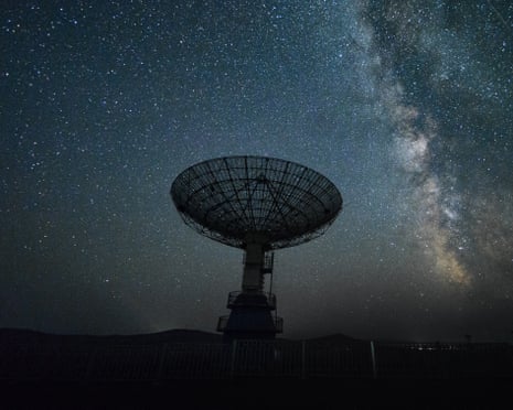 A radio telescope at night with the Milky Way visible