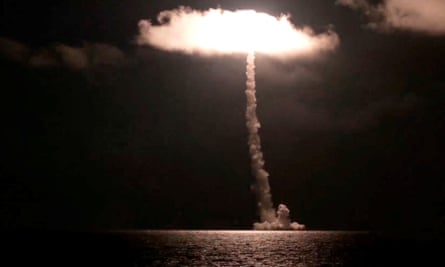 Smoke from a missile launch is illuminated at night over the ocean.