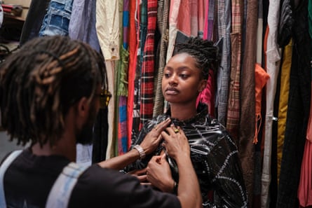 A model is dressed against a backdrop of hanging clothes.