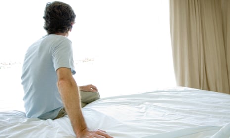 Mature man sitting alone on bed, looking out window