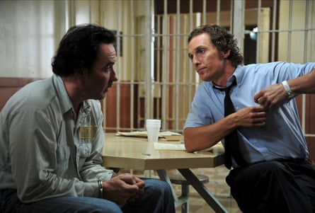 The two men sit at a table in a prison, looking haggard