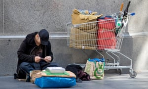 a homeless man on the street with a shopping trolley of belongings