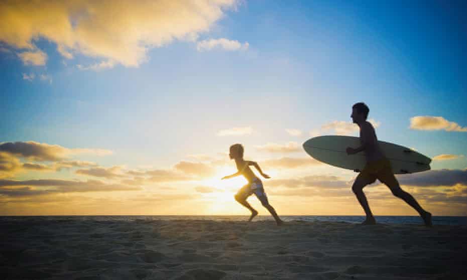 father and son running with surfboard on beach