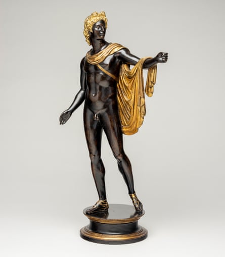 full frontal view of statue depicting standing naked young man with gold cloak draped over his shoulders, gold sandals and gold hair