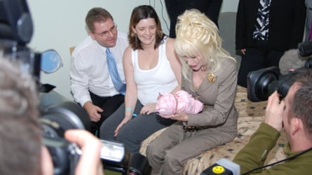 Dolly Parton holds newborn Emma wrapped in pink, beside her seated parents