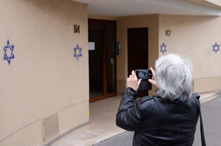 A woman takes pictures of a wall covered with Stars of David painted during the night in the Alesia district of Paris
