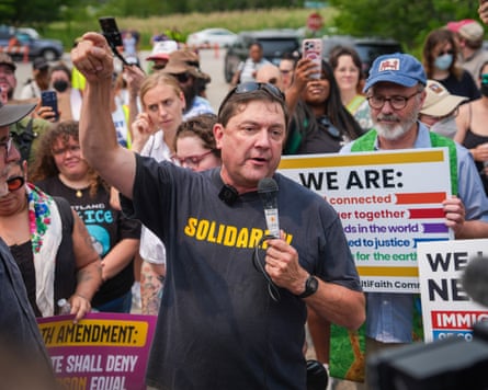 Troy Jackson speaking into a microphone with a crowd of supporters behind him