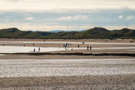 Some people walking on a vast sandy beach with hills in the background