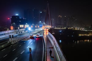 A night-time shot of cars, a motorcyclist and a pedestrian on a bridge