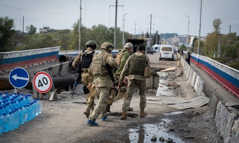 Ukrainians soldiers carry a wounded comrade across a heavily damaged bridge over the Oskil River.