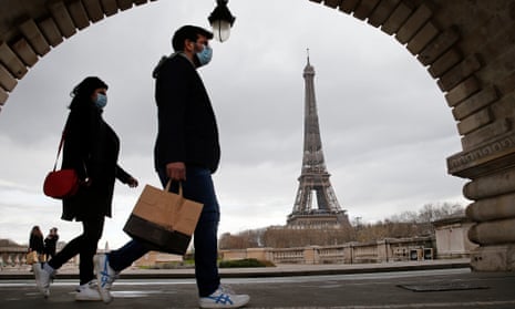 A couple walk past the Eiffel Tower wearing face masks