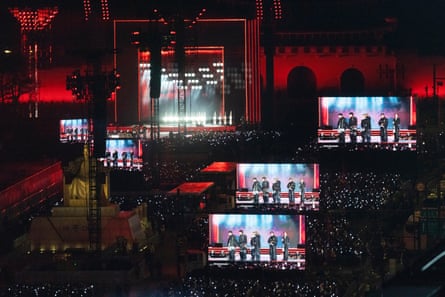 A square lit up in red with five screens showing BTS performing for the crowd