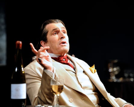 Everett on stage with hair brushed back and a beige suit and red cravat