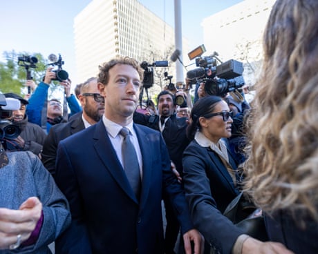 man in suit walks outside while surrounded by people holding cameras