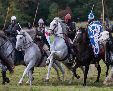 Four people riding atop white and black horses in medieval combat wear holding wooden spears