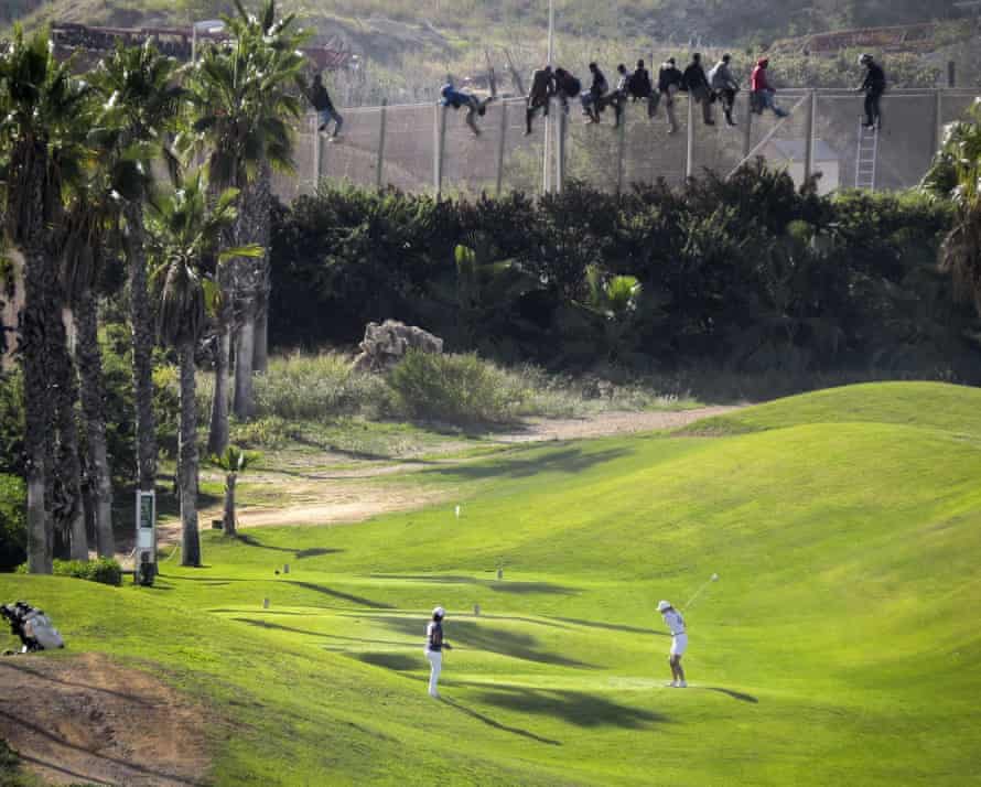 Migrants sit atop a border fence as they attempt to cross into the Spanish enclave of Melilla from Morocco in 2014.