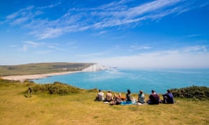 Walkers sitting at the cliff edge looking towards Cuckmere Haven, Seven Sisters country park near Eastbourne, East Sussex, UK