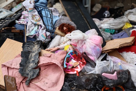 नष्ट हुए घर के मलबे के बीच खिलौने और गुलाबी कपड़ों की एक वस्तु बिखरी पड़ी है।