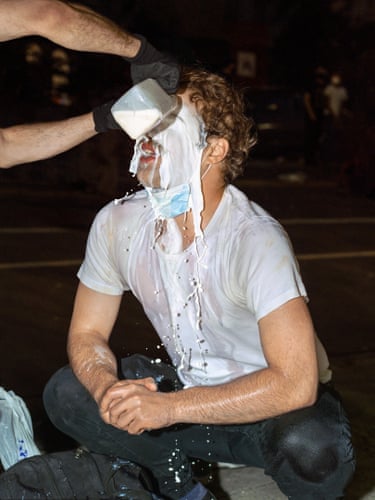 Milk, New York City, 2020. A pair of black gloved hands pour what appears to be a full pint of milk over the face of a moustachioed man