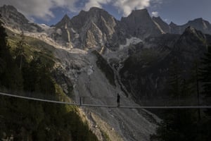 A hiker stands on a suspension bridge with a view of steep mountains