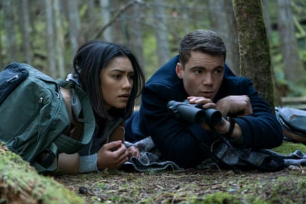 The Night Agent starring Luciane Buchanan and Gabriel Basso lying on the ground in a forest with binoculars