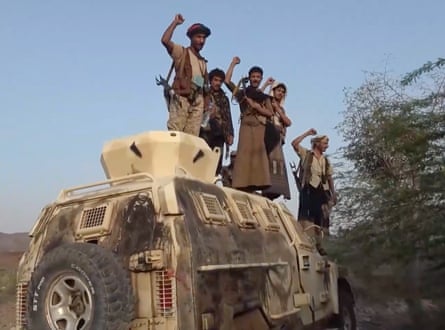 A group of men raise their fists in triumph on top of a milittary vehicle.