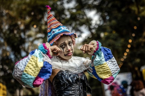 A cosplayer in colourful clown makeup and a striped hat gestures with fists raised at a convention