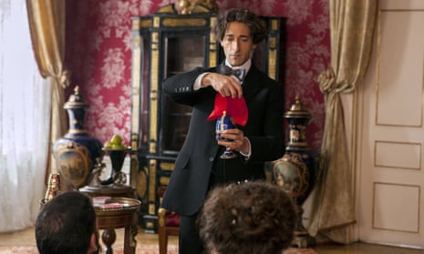 Adrien Brody holding a red handkerchief over a vase, conducting a trick
