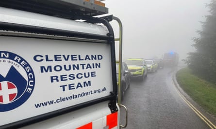A row of emergency services vehicles parked on a road in foggy conditions