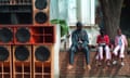 A man and two children sit on a wall with a wall of speakers to their left