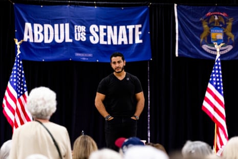 Abdul El-Sayed stands on stage listening, in front of a "Senate" campaign banner and flags