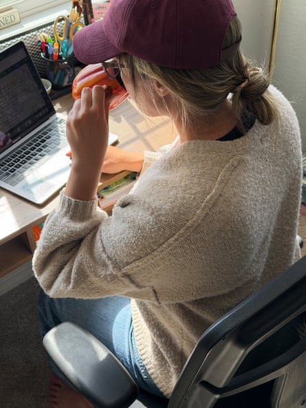 a woman in a baseball cap and cardigan sipping coffee while working on computer