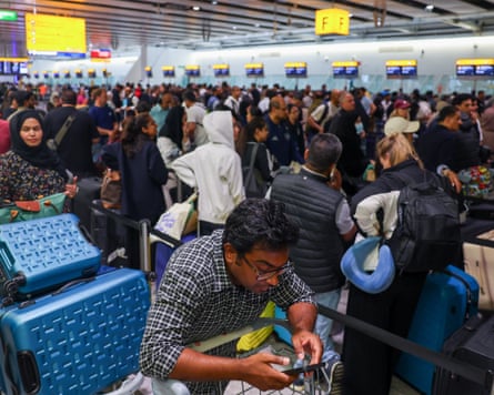 A man uses a smartphone as people queue to check in at Heathrow airport