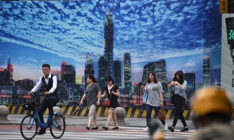 People crossing a road in front of a billboard on the wall of a construction site in Beijing’s central business district. 
