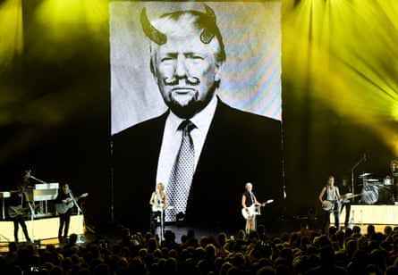 The Chicks performing on stage against a large backdrop of a Donald Trump picture graffitied with devil’s horns and facial hair